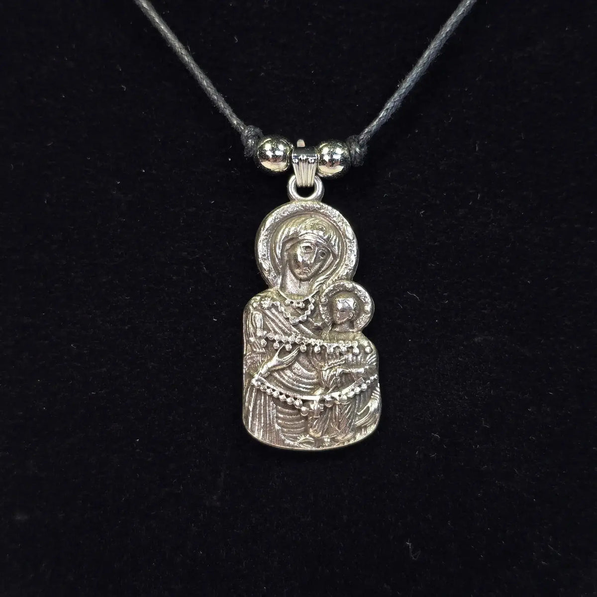 Silver pendant of a religious figure on a black cord against a black background
