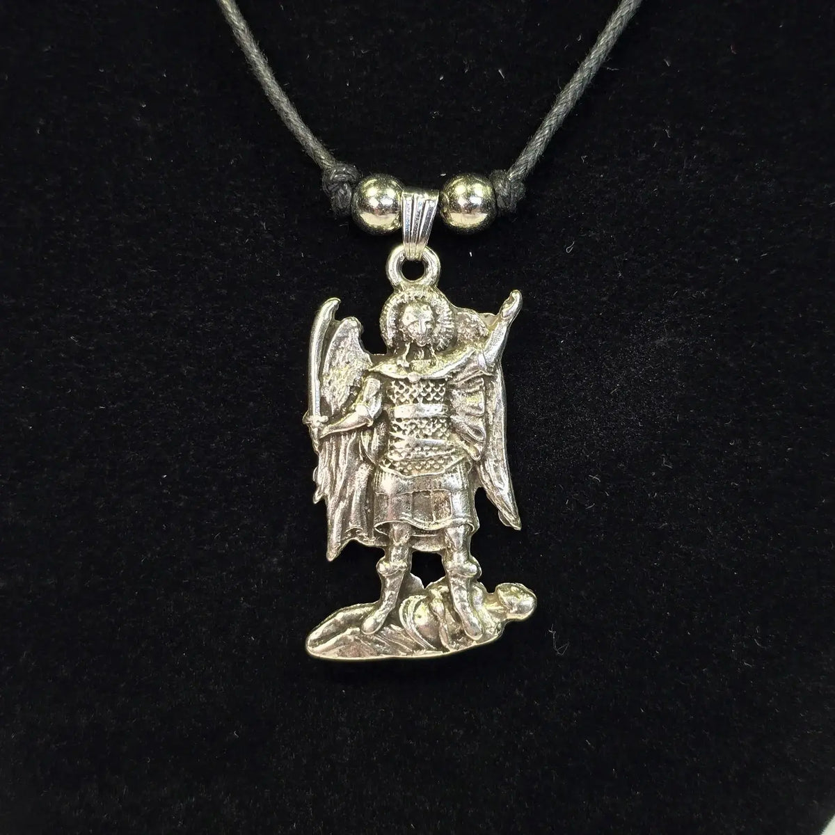 Silver angel pendant on a black cord against a black background